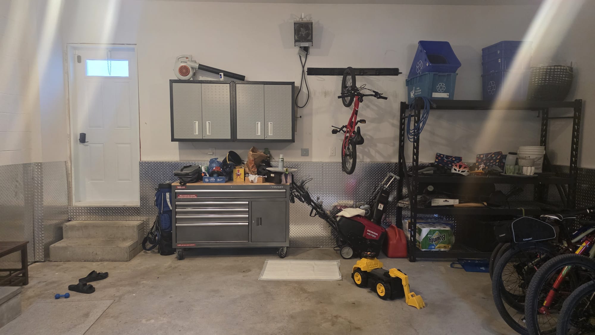 Cluttered garage wall with exposed bikes, bins, shelving and tools